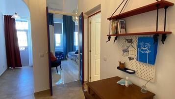 Una habitación con una mesa de comedor de madera, un panel de corcho con diversos objetos, y vistas a otra habitación con una cama y cortinas.