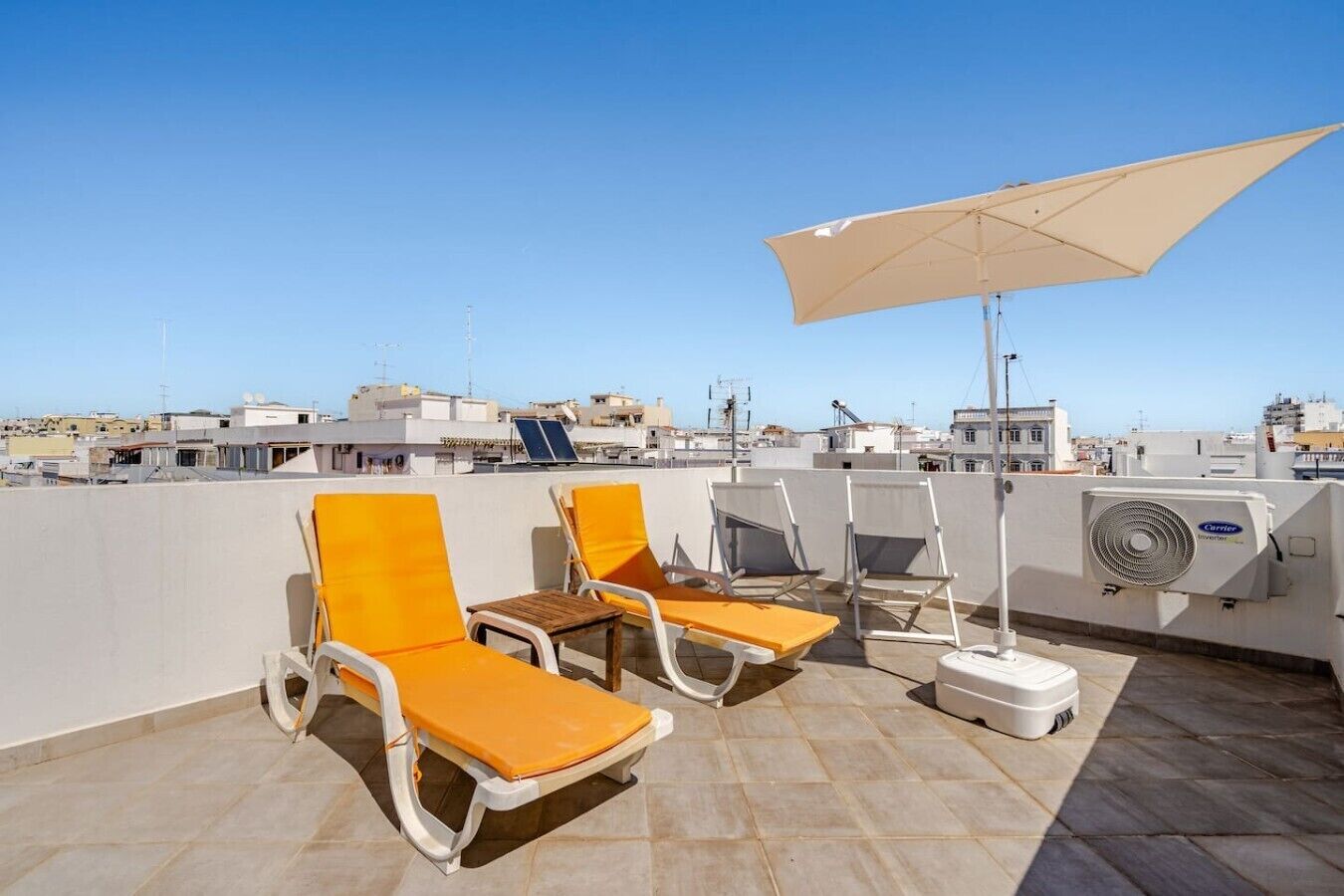 En tagterrasse med liggestole og en stor parasol med udsigt over bybilledet.
