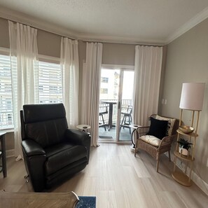 A modern living room with a black leather sofa, a wicker chair, a small round table, and a floor lamp. - Modern 1BR Beachfront Condo & Beautiful Courtyard Pool - D43 Orange Beach AL (Orange Beach)