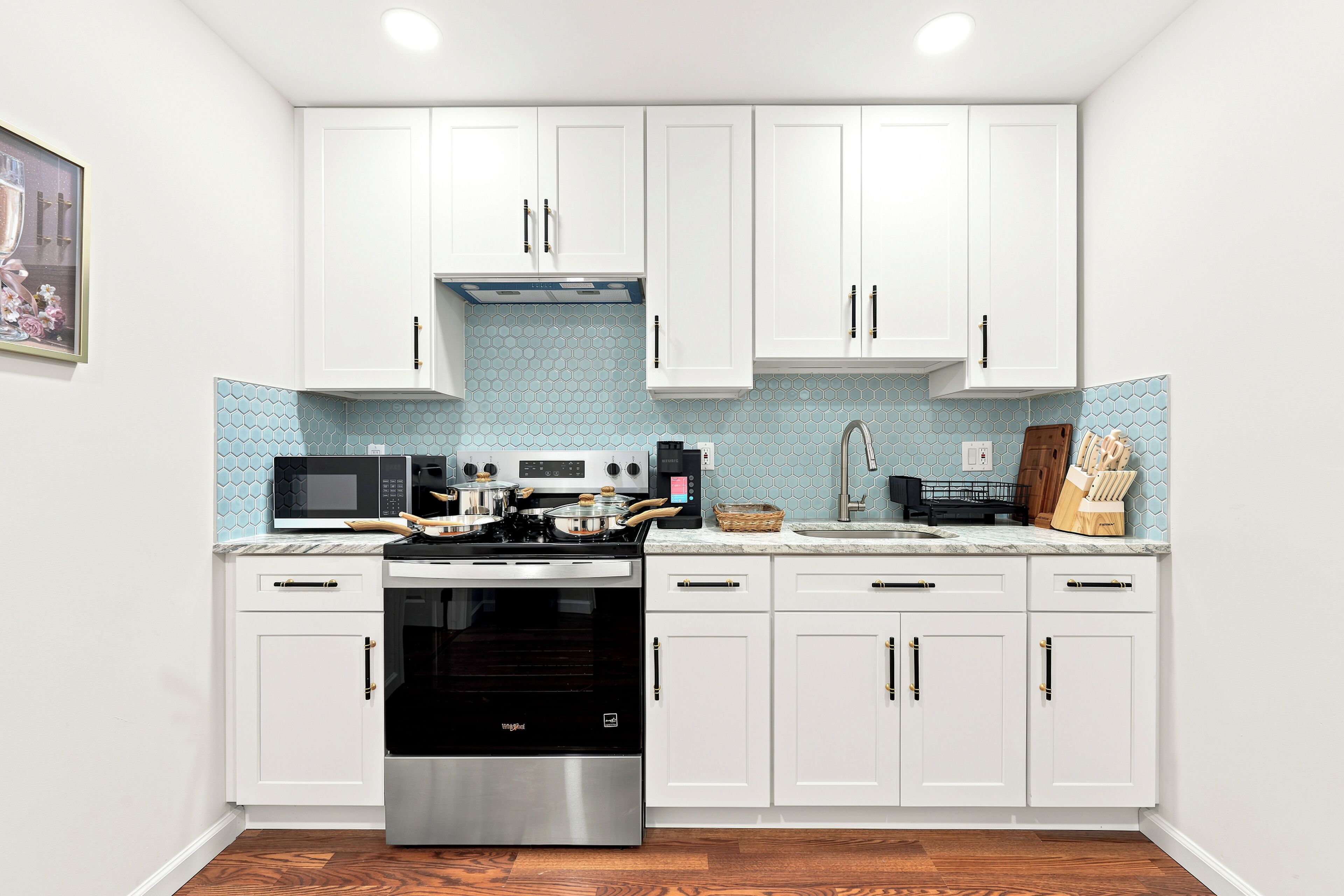A kitchen with white cabinets, a stainless steel stove, a microwave, and a sink.
