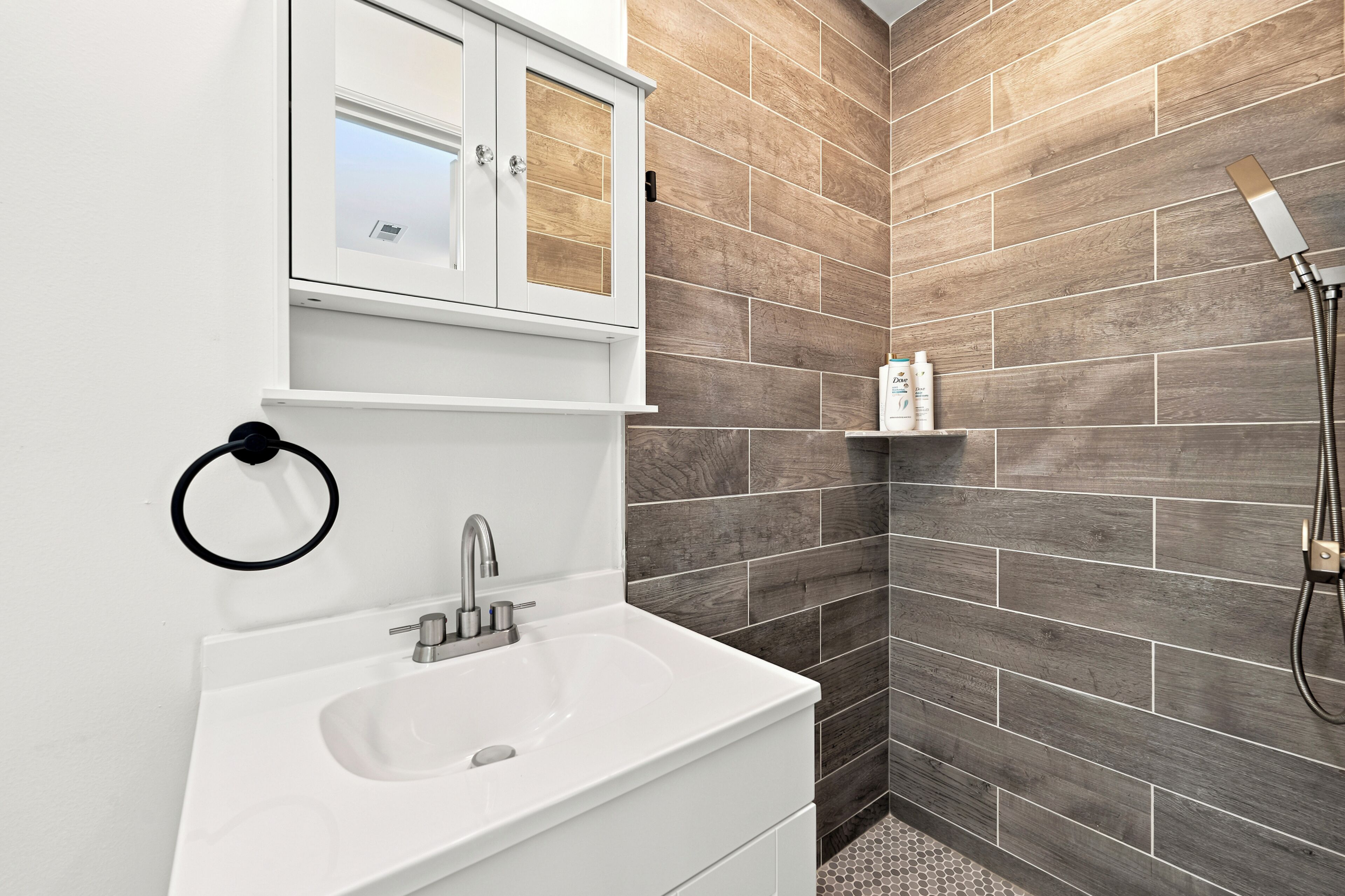 A bathroom with a white sink, a mirror, and a shower area with a hose.