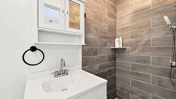 A bathroom with a white sink, a mirror, and a shower area with a hose.