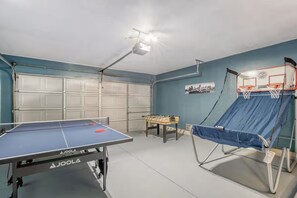 A room with a ping pong table, a foosball table, and a basketball hoop. - Family Retreat • King Suite • Sleeps 11 • Game Room • Near SeaWorld & Lackland (San Antonio)