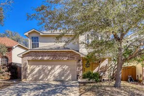 A two-story house with a garage, a front yard with a tree, and a brick entrance. - Family Retreat • King Suite • Sleeps 11 • Game Room • Near SeaWorld & Lackland (San Antonio)
