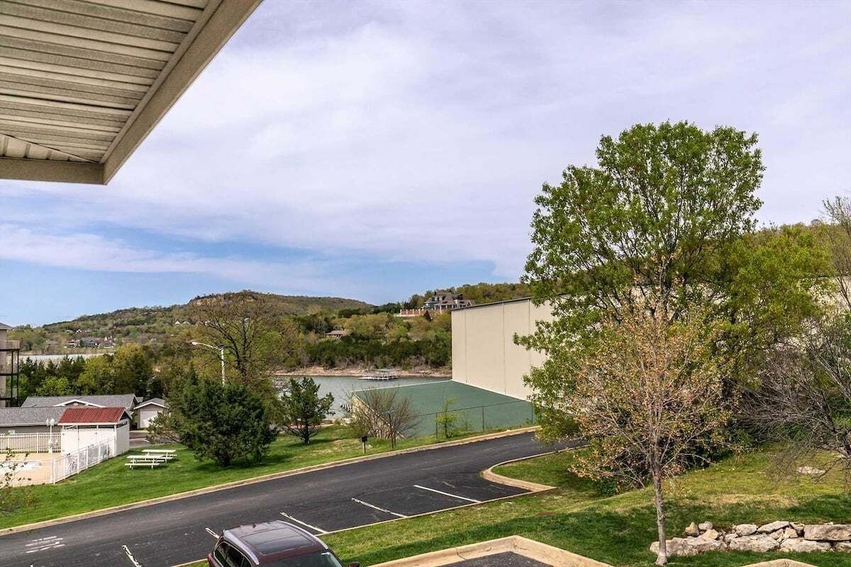 Un aparcamiento con una carretera que conduce a un edificio, rodeado de vegetación y vistas a un lago.