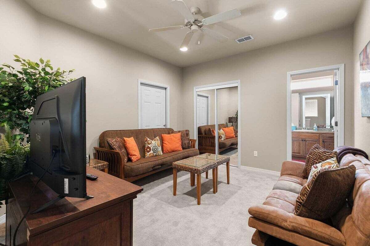 A living room with a flat-screen TV, two couches, a coffee table, and a ceiling fan.