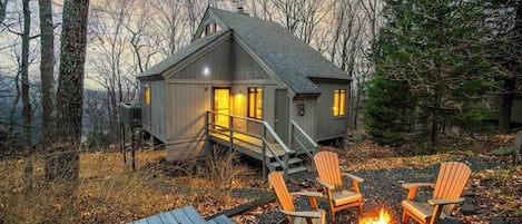 A cabin with a deck, outdoor seating, and a fire pit.