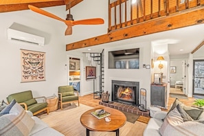 Ein geräumiges Wohnzimmer mit Kamin, Deckenventilator und einer Treppe zu einer oberen Etage.