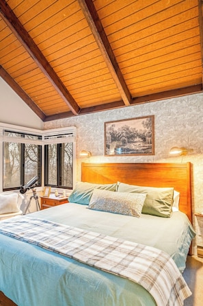 A bedroom with a large bed, wooden ceiling beams, a nightstand, a telescope, and a framed picture on the wall. - Walk to SKi Slopes  and Hot Tub (Wintergreen Resort)