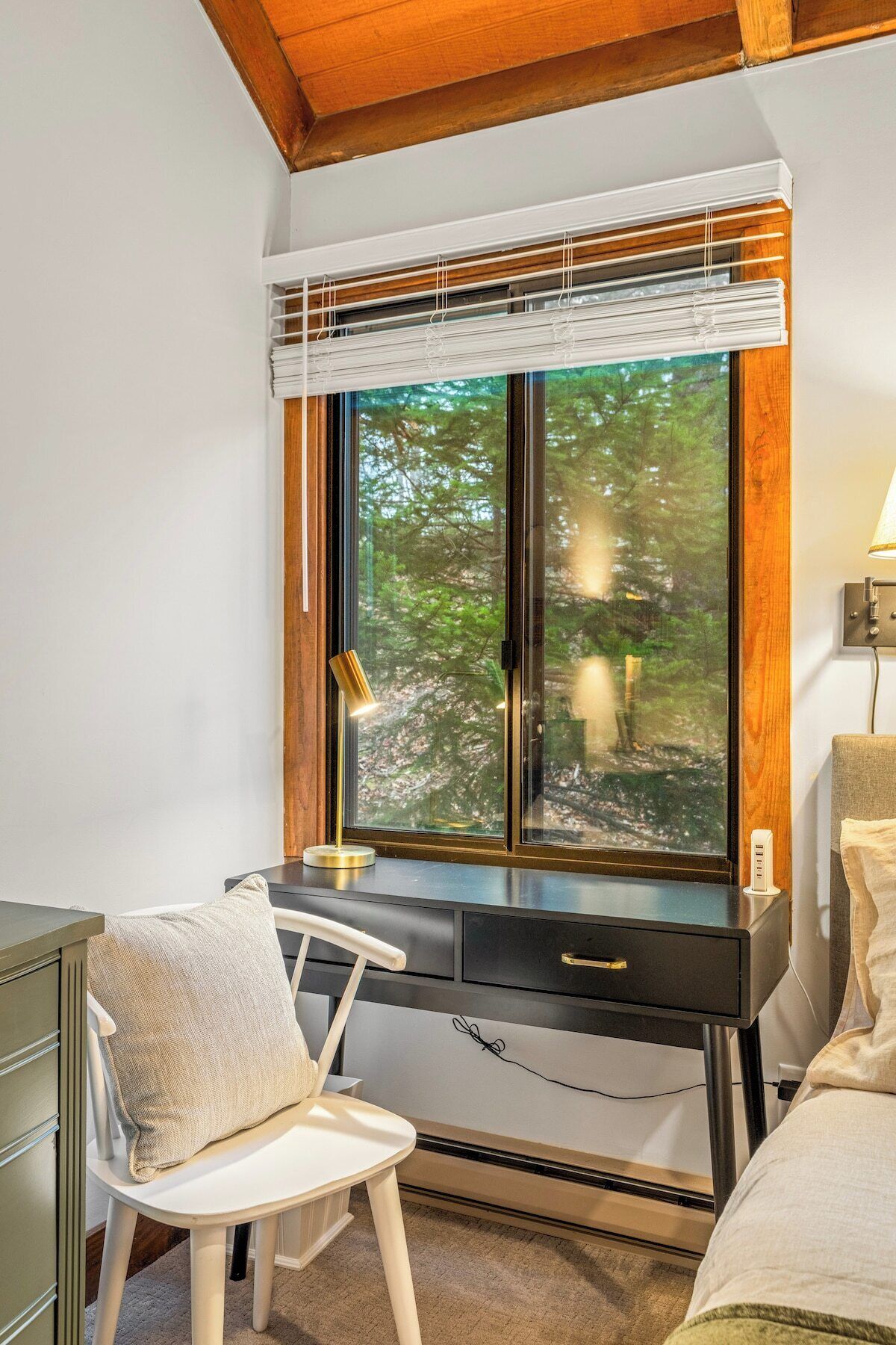 A room with a desk, chair, and a large window with a view of trees.
