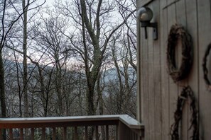 Eine Holzterrasse mit Geländer, ein Kranz an der Wand und bewaldeter Hintergrund.