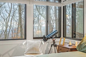 A bedroom with a telescope on a tripod, a framed certificate, and a small statue on a bedside table.