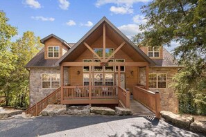 A two-story lodge with a stone facade, a wooden deck, and a staircase leading to the entrance. - Private Lodge near Silver Dollar City_Ramp Entry_Overlooks Golf Course_Free Attraction Tickets (Branson West)