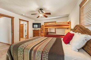 Ein Schlafzimmer mit Etagenbett, Deckenventilator, Fernseher und einem gemusterten Bettbezug.