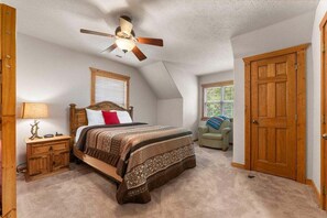 Une chambre à coucher comprenant un lit, une table de chevet, une lampe, un ventilateur de plafond, une fenêtre et une porte.