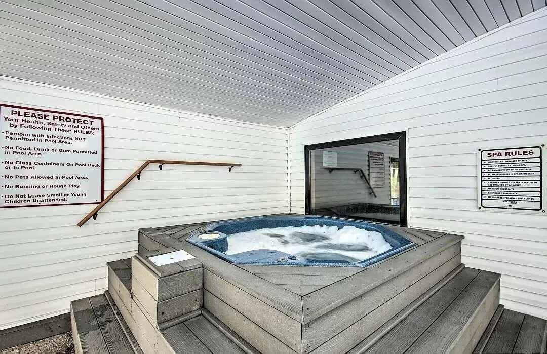 A hot tub with a wooden deck, a sign listing pool rules, and a spa rules sign.
