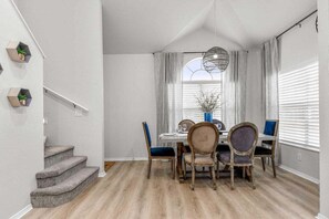 Ein Essbereich mit Tisch für vier Personen, einer Treppe und einem mit Vorhängen versehenen Fenster.
