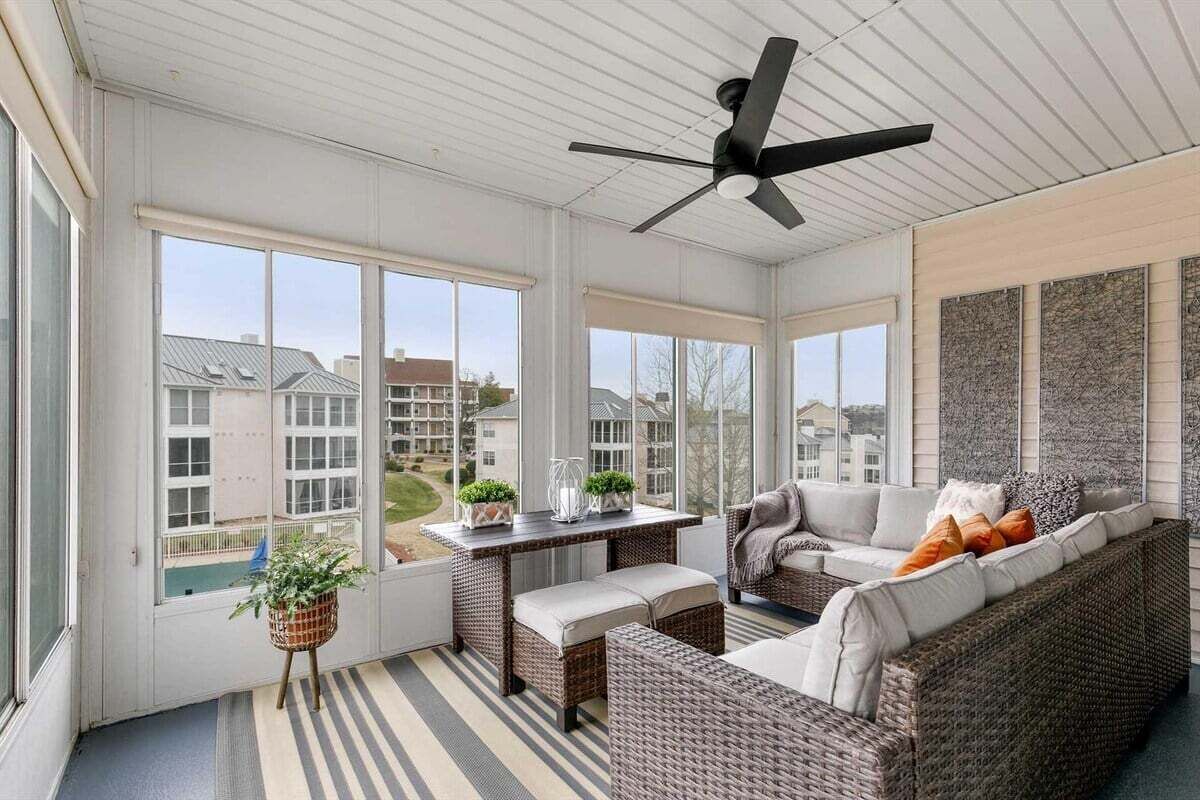 A sunroom with wicker furniture, a ceiling fan, and large windows offering a view of a residential area.