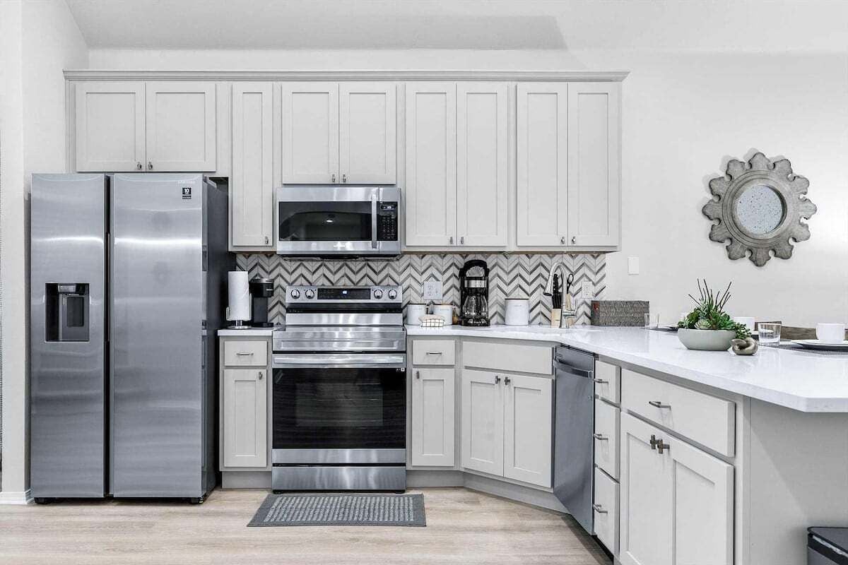 A modern kitchen with white cabinets, stainless steel appliances, and a herringbone tile backsplash.