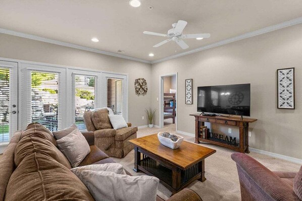 A living room with a sofa, armchairs, a coffee table, a TV, and a ceiling fan. - Table Rock Lake - Emerald Pointe - Walk In Condo w Lake and Pool Access- Free Daily Tickets (Hollister)