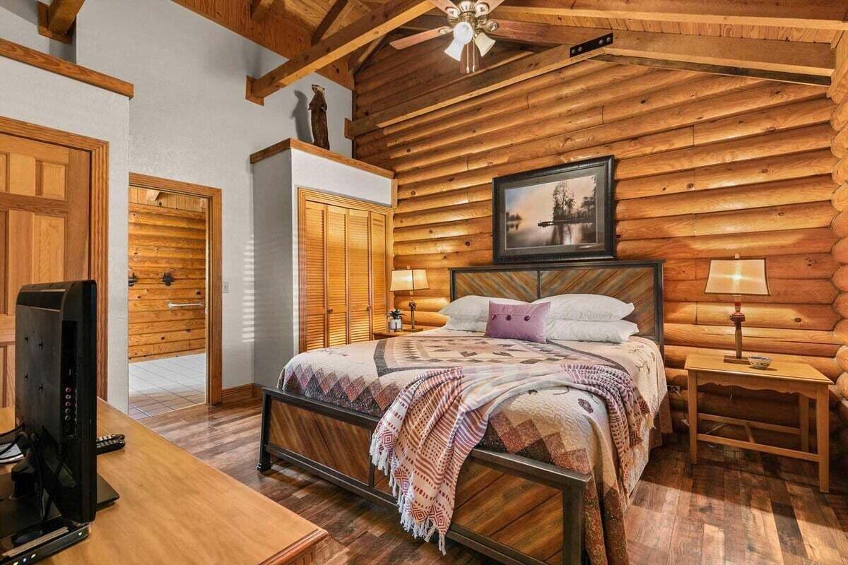 A log cabin-style bedroom with a bed, bedside lamps, and a television.