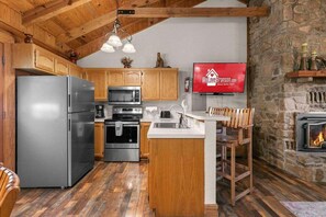 A kitchen with wooden cabinets, stainless steel appliances, a stone wall, and a fireplace. - Genuine Log Cabin with Fireplace, Whirlpool Tubs, Onsite Amenities, Free Daily Attraction Tickets (Branson)