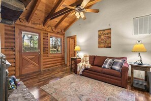 A log cabin interior with a wooden ceiling, a brown sofa, two lamps, and a wall with a love quote. - Genuine Log Cabin with Fireplace, Whirlpool Tubs, Onsite Amenities, Free Daily Attraction Tickets (Branson)