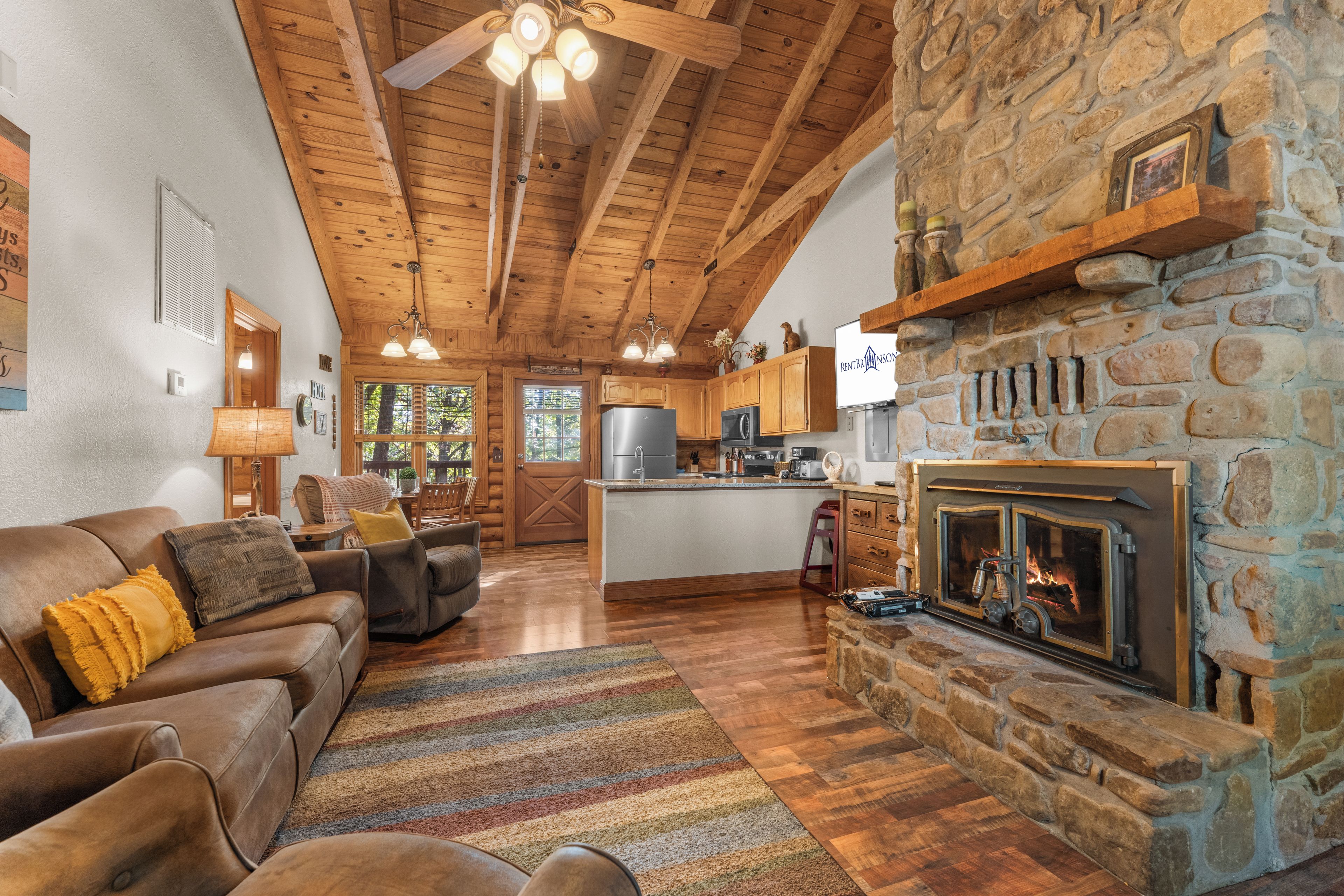 A cozy living room with a fireplace, wooden ceiling, and a stone wall.