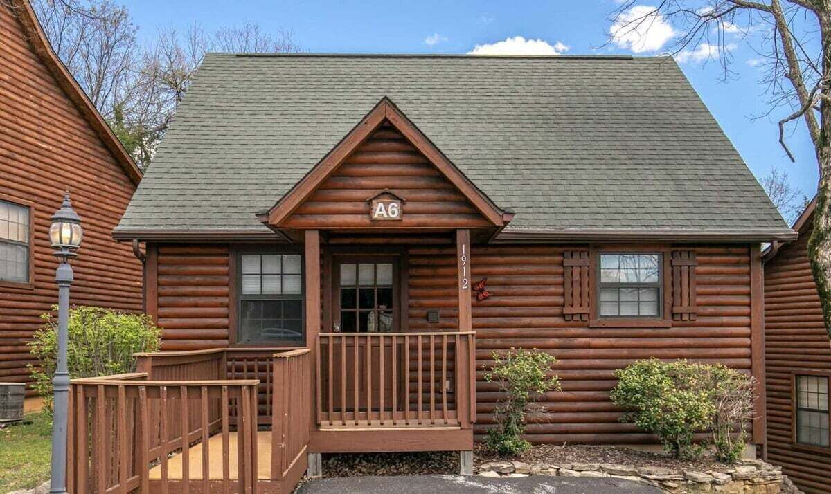 A log cabin with a front porch, a number plaque, and a small garden.