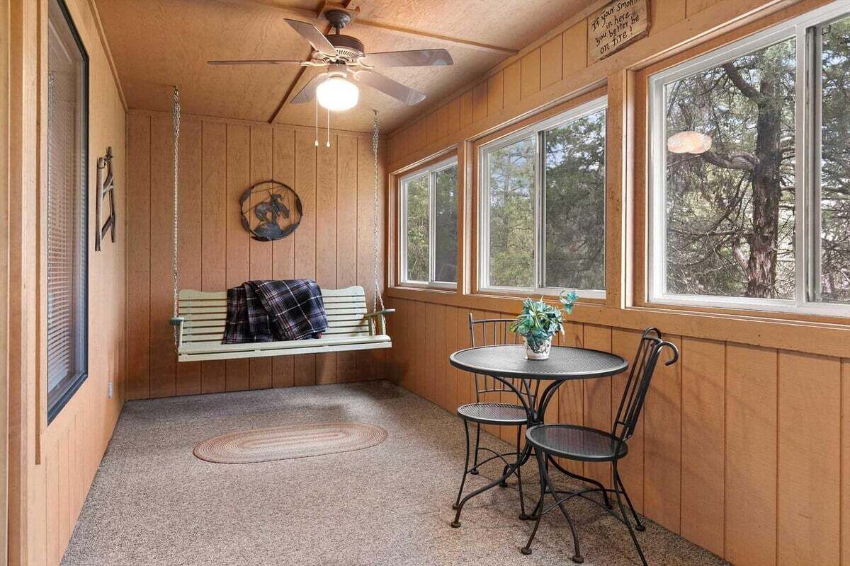 Une pièce chaleureuse avec un décor intérieur en bois, un ventilateur de plafond, un banc, une petite table avec des chaises et de grandes fenêtres.
