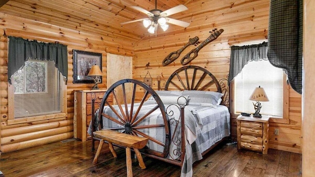 Un dormitorio tipo cabaña de troncos con una cama de madera, un ventilador de techo y decoración rústica.