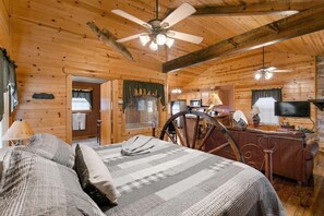 A cozy cabin interior with a bed, a desk, a television, and a ceiling fan.