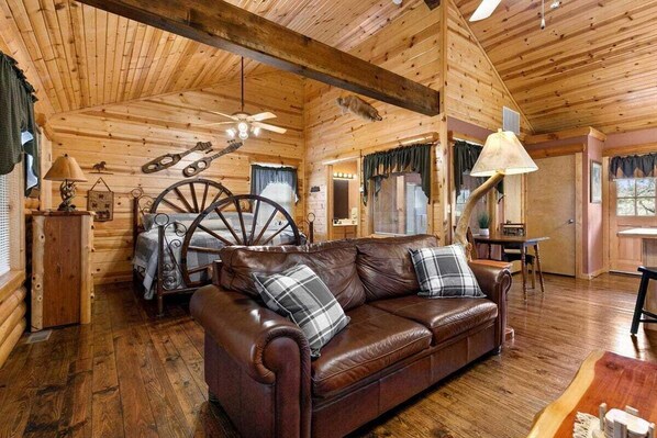A cozy cabin interior with a leather sofa, wooden walls, and a ceiling fan.
