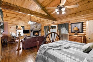 A log cabin interior with a fireplace, a bed, a desk, and a chair.