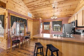 A wooden cabin interior with a kitchen area featuring a bar counter, stools, and modern appliances.