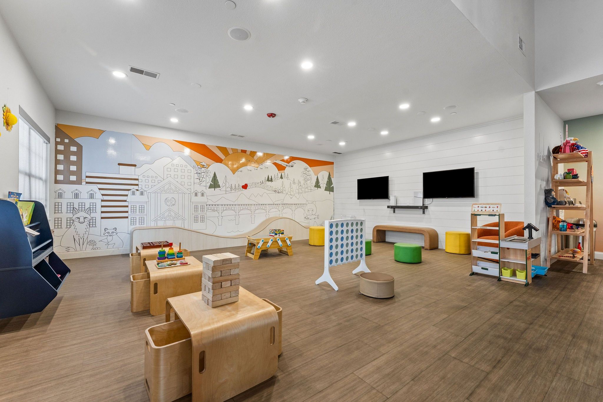 A children's playroom with wooden furniture, a mural, and a television.