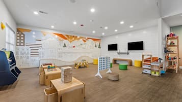 A children's playroom with wooden furniture, a mural, and a television.