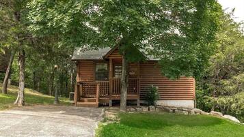 A log cabin with a porch, surrounded by trees and a grassy area.