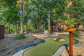 Un campo de mini golf con un recorrido sinuoso, estructuras de madera y un fondo de árboles y edificios.