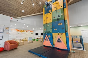 An indoor climbing area with a padded landing area, climbing walls, and a mural on the wall.