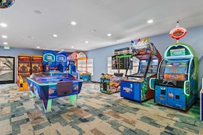 A room with arcade games, including basketball and baseball machines, carpeted flooring, and a ceiling with recessed lighting.