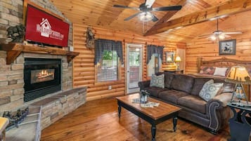 A log cabin interior with a fireplace, a leather sofa, a coffee table, and a ceiling fan.
