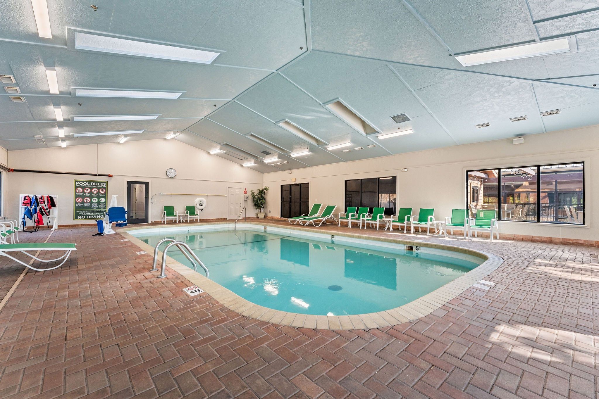 Una piscina interior con agua cristalina, rodeada de sillones de descanso y un suelo de ladrillo.