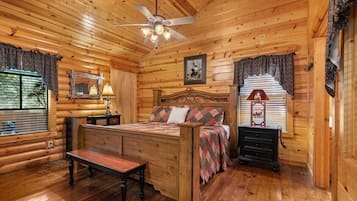 A log cabin bedroom with a wooden bed, a bench, a nightstand, and a ceiling fan.