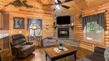 A log cabin interior with a fireplace, a ceiling fan, and a television mounted above it.