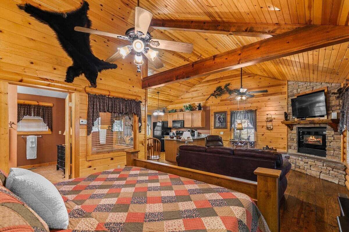 Ein Holzblockhaus-Interieur mit Kamin, Deckenventilator, Küchenzeile und einer gemütlichen Sitzecke.
