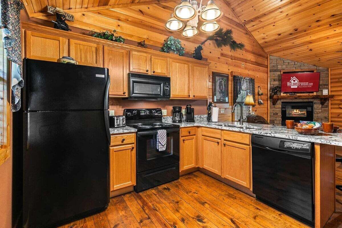 Una cocina con armarios de madera, un refrigerador negro, un microondas, una estufa y un lavavajillas.