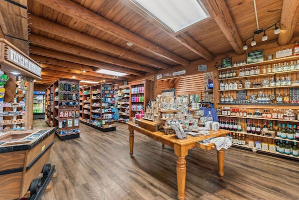 A wooden interior with a central table displaying various items, shelves stocked with bottles, and a 'Peace, Love, Country Music' sign.