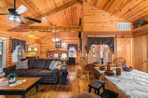 A log cabin interior with a living room, dining area, and a kitchen.