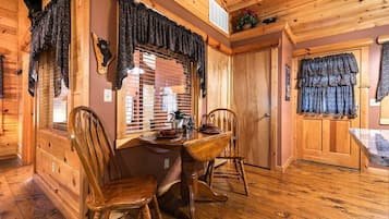 A wooden interior with a dining area featuring a table and chairs, a window with blinds, and a door with a curtain.